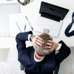 uomo seduto davanti al computer con la testa tra le mani