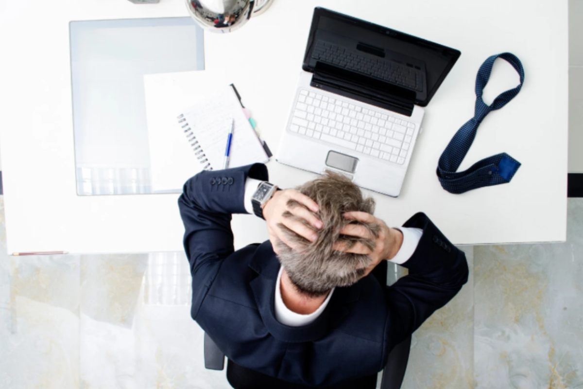 uomo seduto davanti al computer con la testa tra le mani